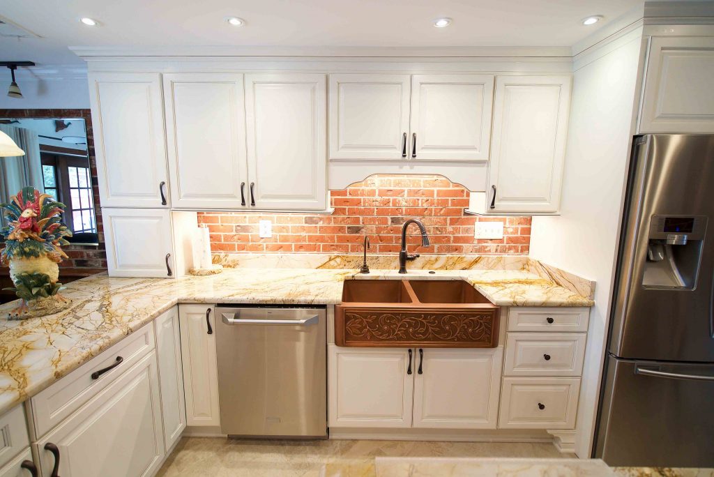 A kitchen with white cabinets and a brick wall.