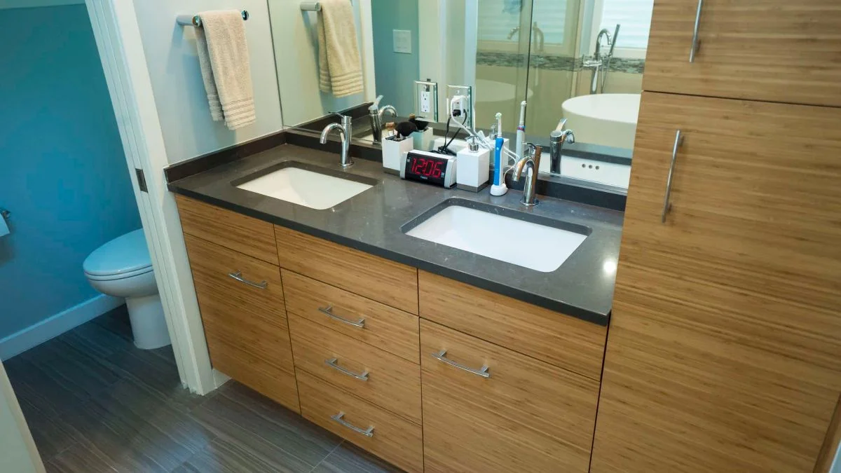 Double-sink bathroom vanity with bamboo cabinets, dark countertop, and chrome faucets