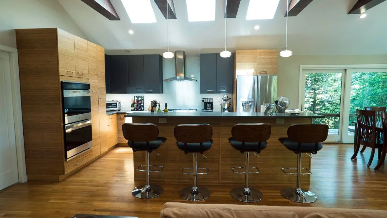 Modern kitchen with bamboo slab cabinets, dark wall cabinetry, and a large island with seating under skylights