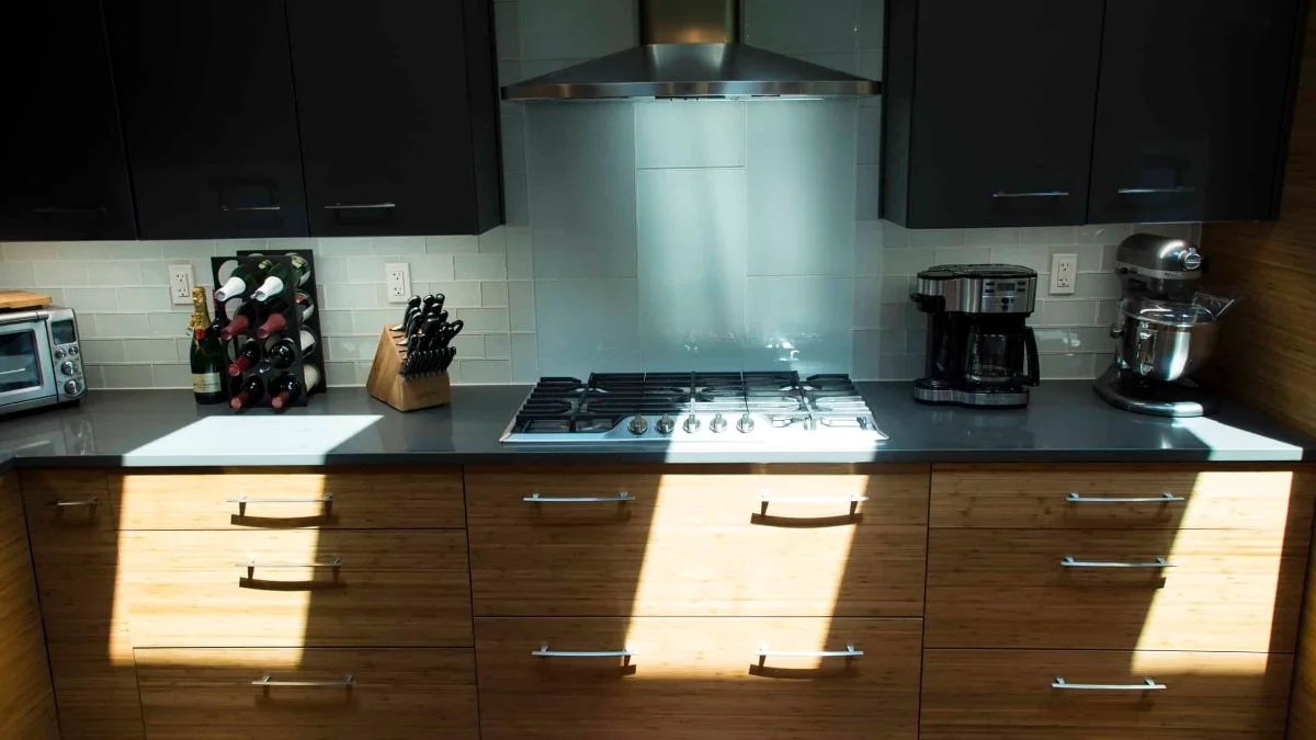Gas cooktop with stainless steel hood, gray backsplash, and bamboo slab base cabinets in a modern kitchen