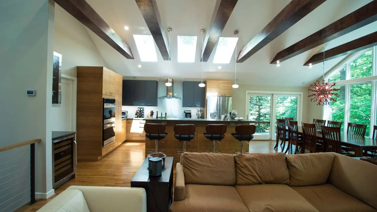 Open-plan interior with modern kitchen, large island seating, exposed ceiling beams, and skylights