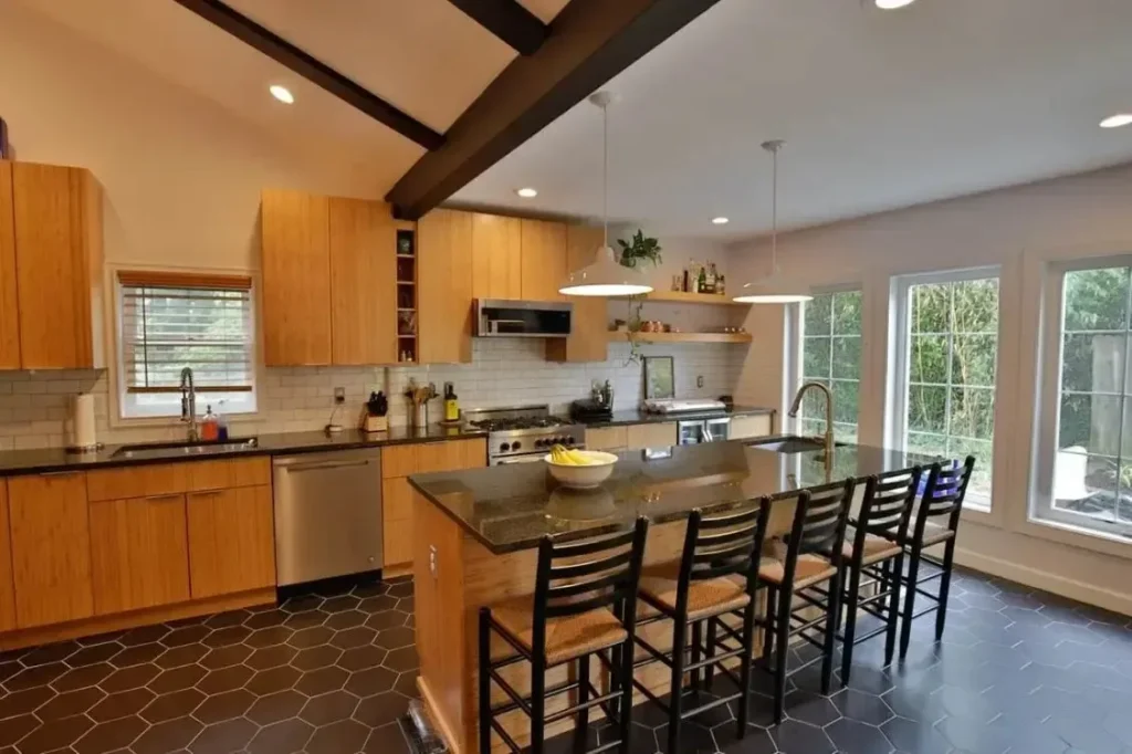 Wide kitchen view with wood cabinets, island seating, open shelving, and black hex tile flooring.
