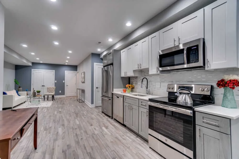 45 Kitchen Remodeling Ideas for 2026 | USA Cabinet Store 26 Transitional kitchen with white and grey cabinetry, stainless steel appliances, and a view into a modern living room.