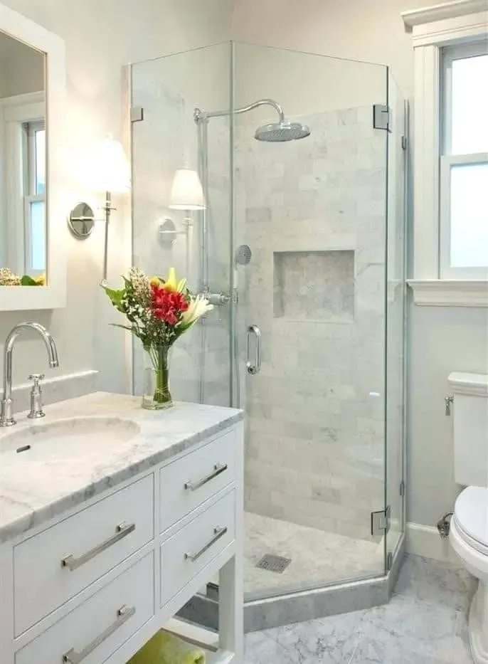 White bathroom vanity with marble-look countertop and frameless glass walk-in shower featuring a rain showerhead and recessed wall niche