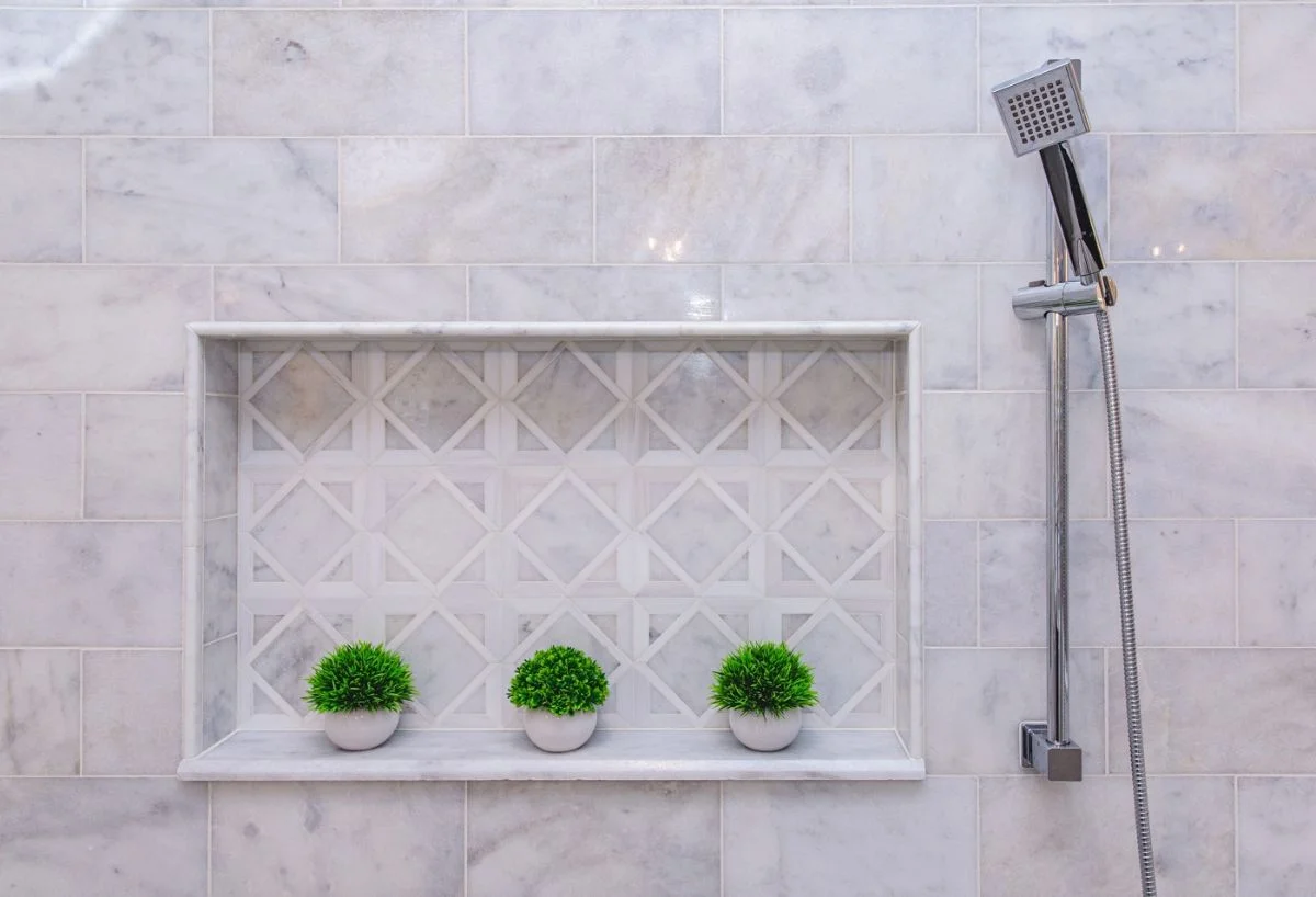 Recessed marble shower niche with geometric mosaic backing and chrome handheld showerhead in Ashburn VA.