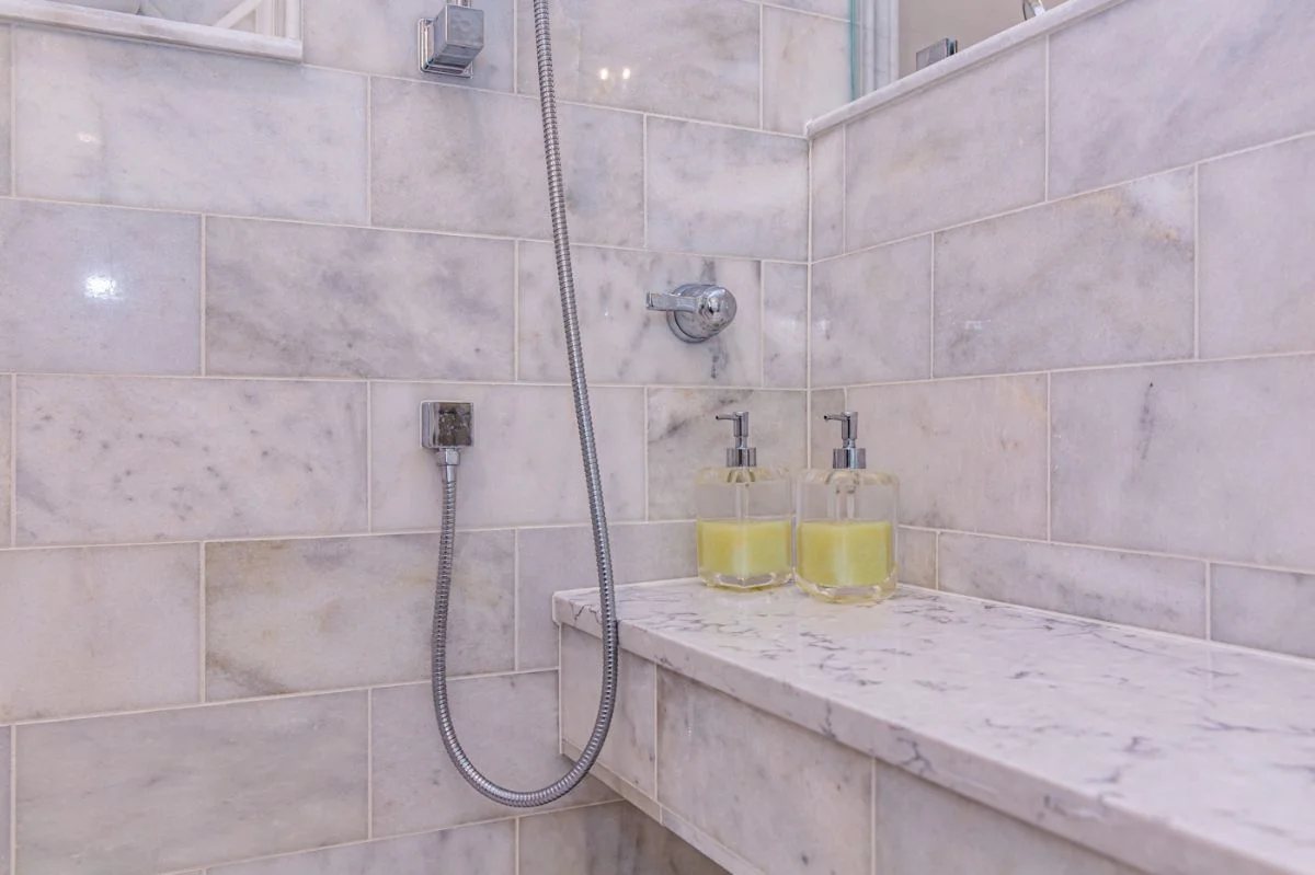 Marble shower bench with chrome handheld sprayer connection in an Ashburn VA bathroom remodel.