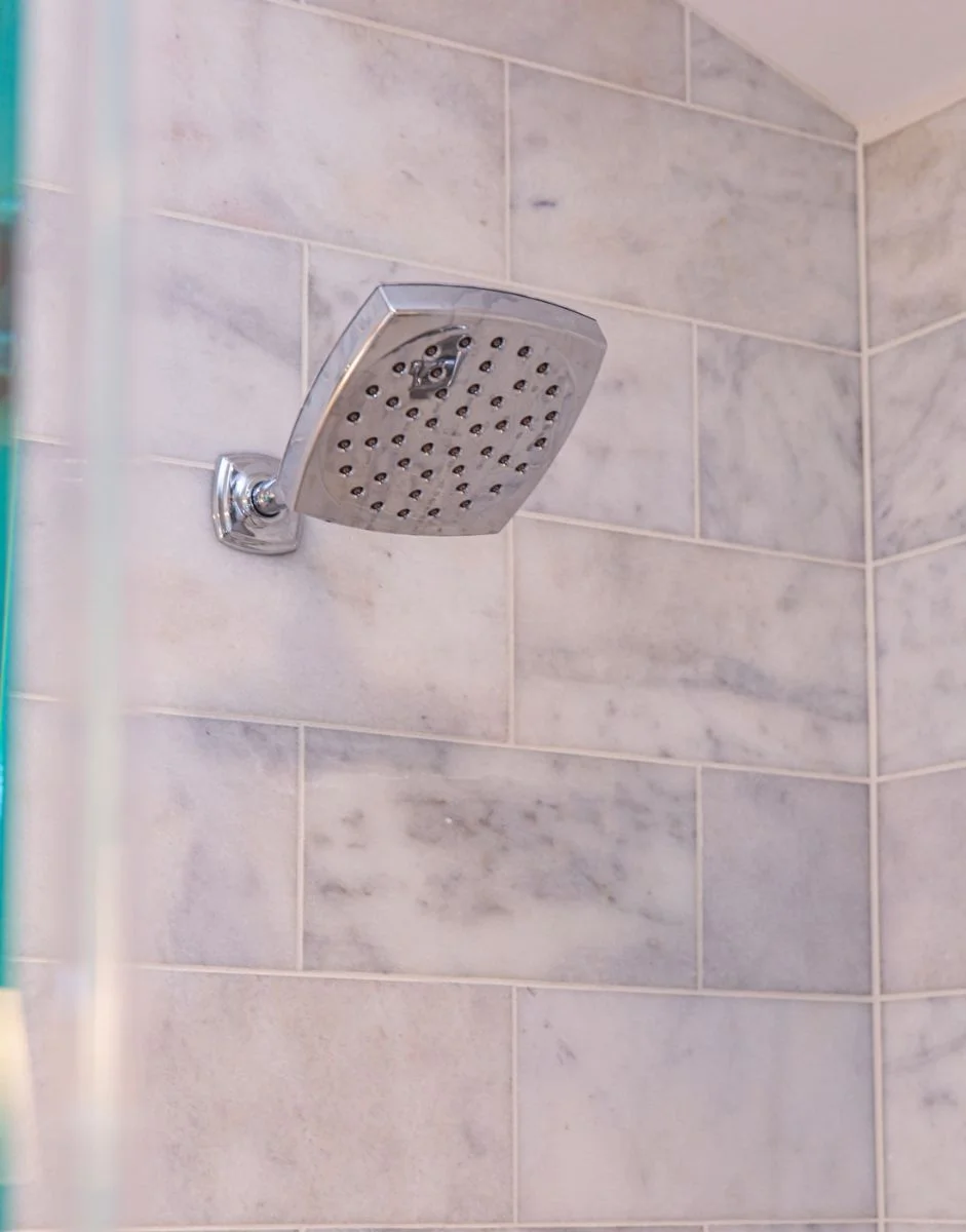 Modern square chrome wall-mounted showerhead on marble subway tile in an Ashburn VA bathroom.