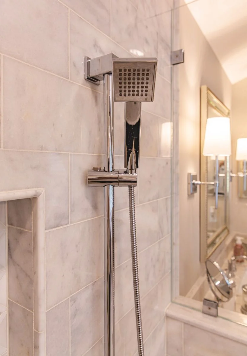 Modern chrome handheld showerhead on slide bar in marble walk-in shower Ashburn VA.