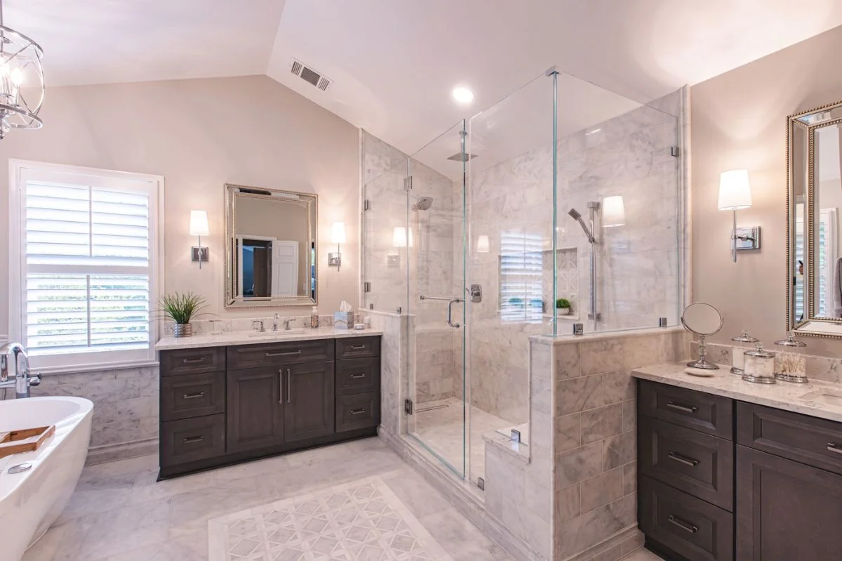 Luxury master bathroom in Ashburn VA featuring a glass walk-in shower, double dark wood vanities, and marble floors.