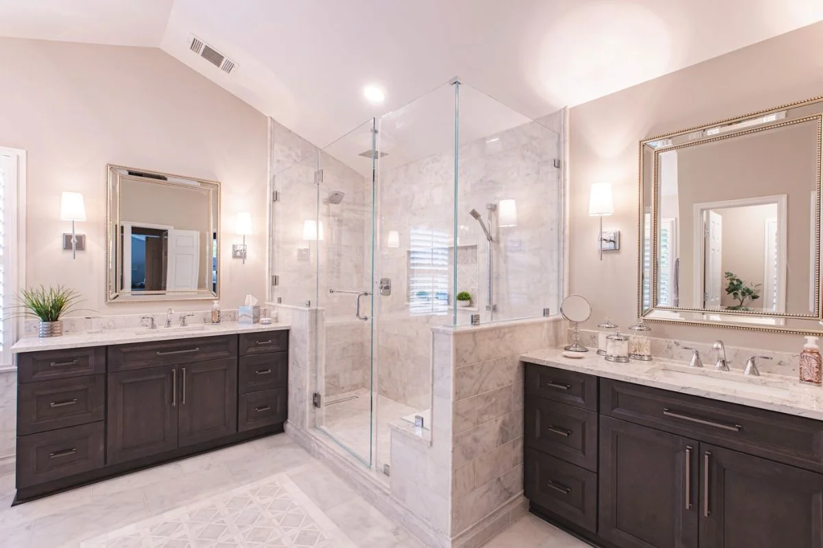 Symmetrical Ashburn VA bathroom with double dark wood vanities and a central marble walk-in glass shower.