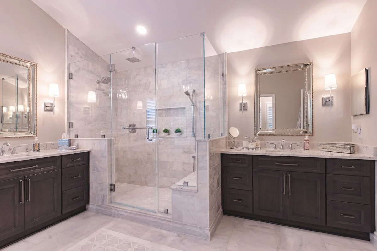 Symmetrical Ashburn VA bathroom with double dark wood vanities and a central marble walk-in glass shower.