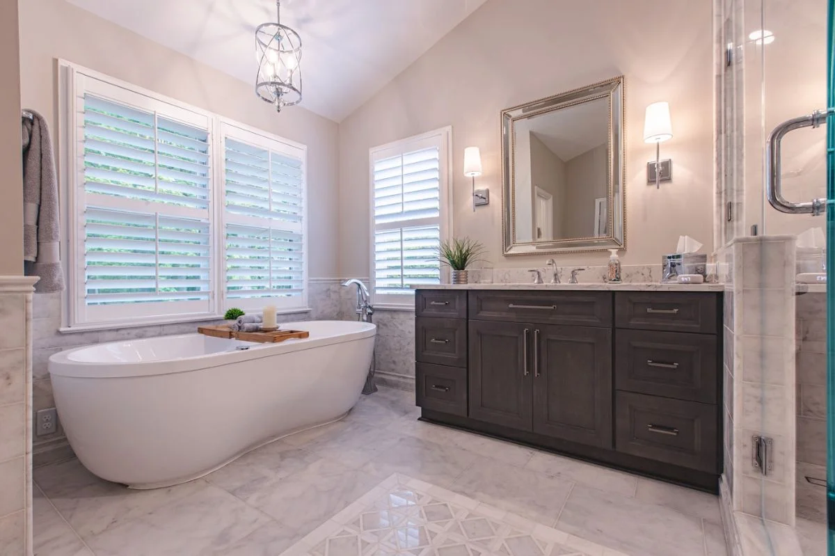 Luxury master bathroom in Ashburn VA with freestanding tub, dark wood vanity, and marble tile flooring.