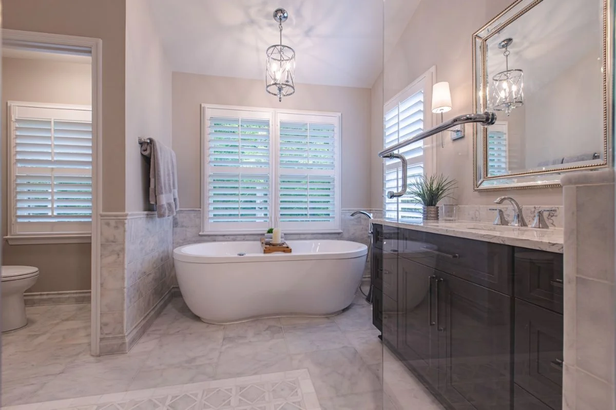 Master bathroom in Ashburn VA with freestanding tub, dark wood vanity, marble tile, and plantation shutters.