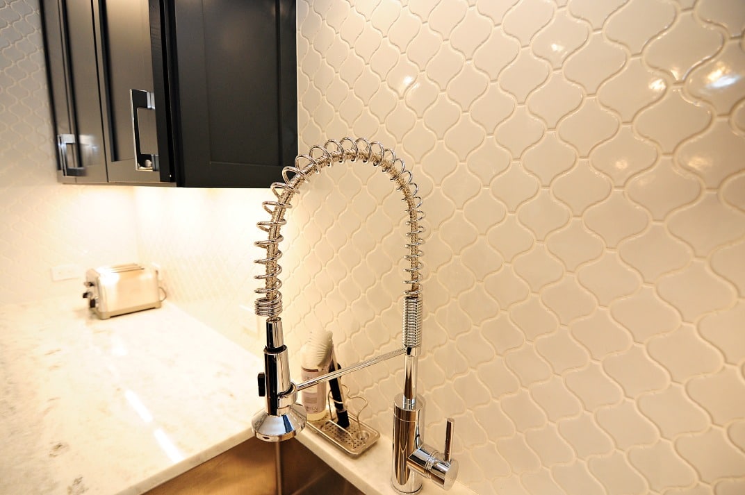 A kitchen sink with a faucet and a white tile wall