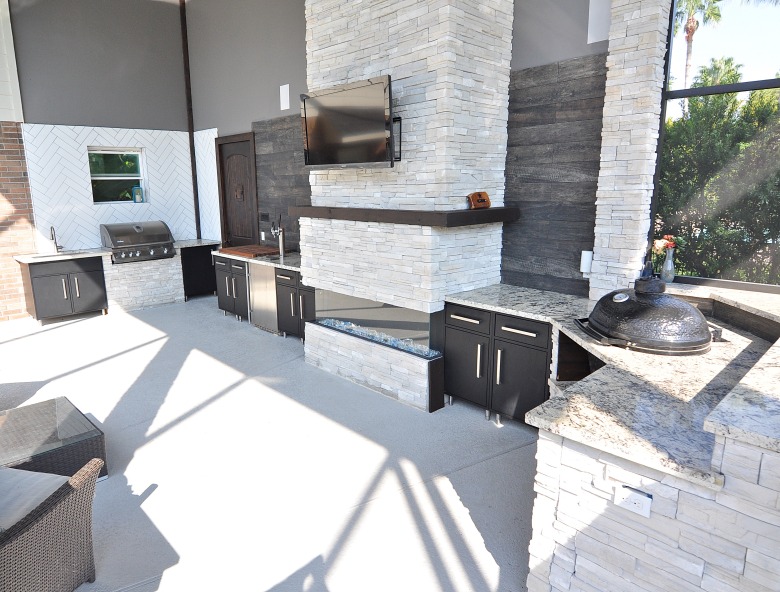 A spacious outdoor kitchen featuring a fireplace and a TV