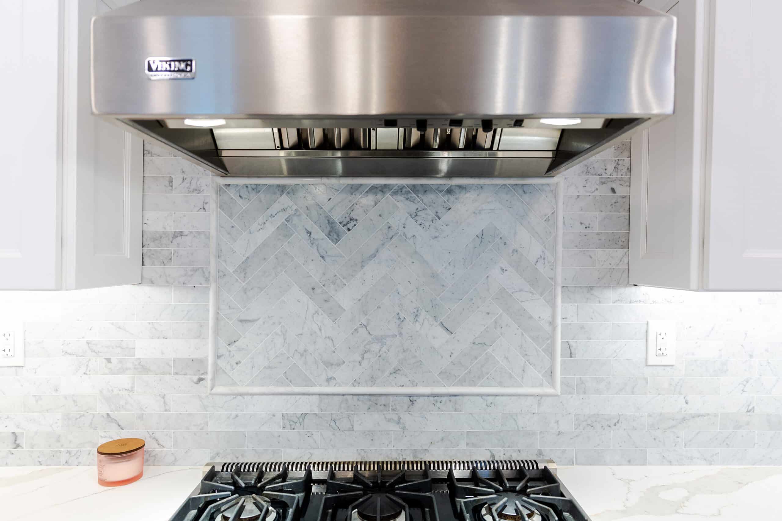 A kitchen with a sleek stainless steel hood and a luxurious marble backsplash