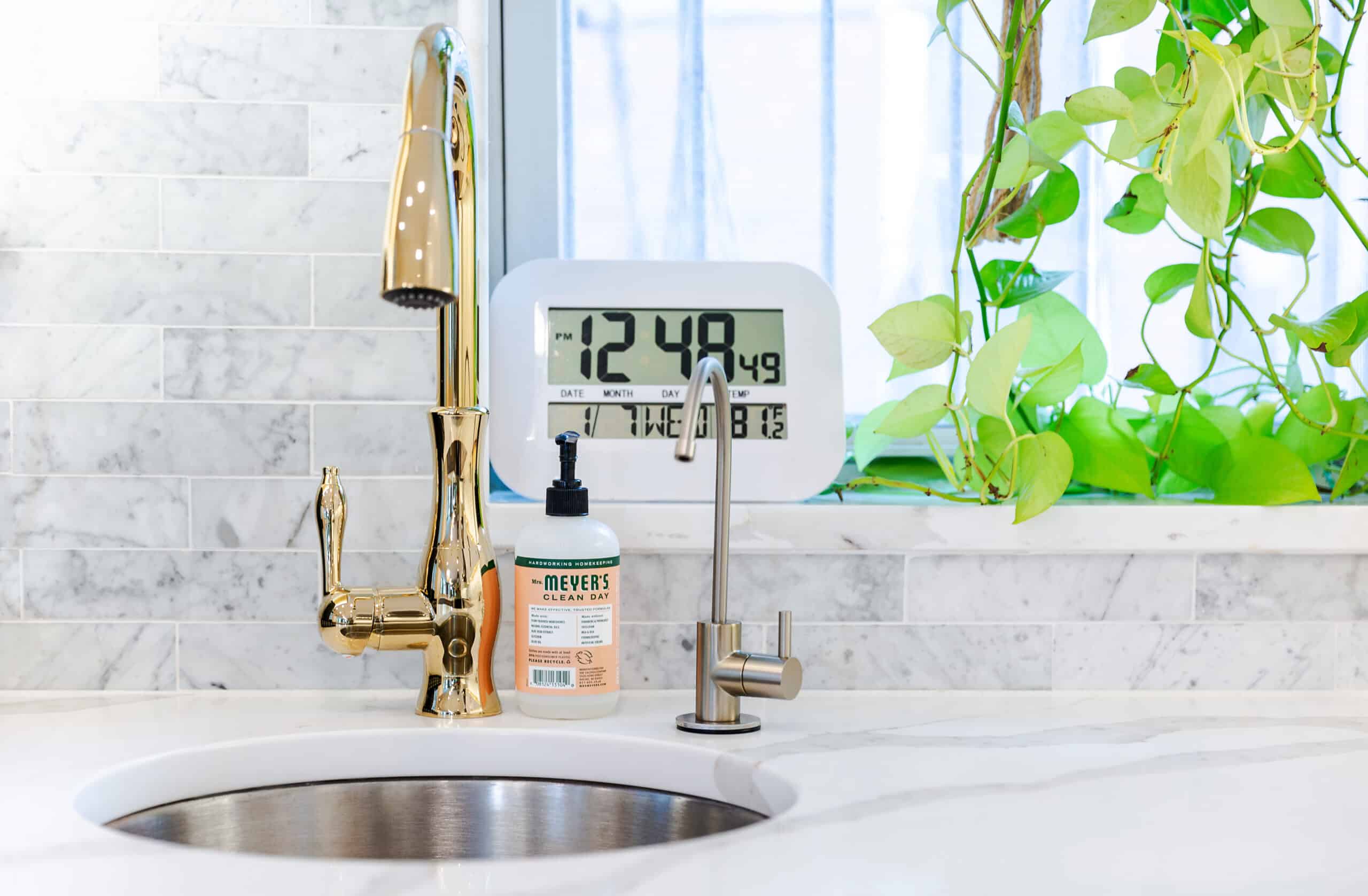 A kitchen sink with a clock and a faucet
