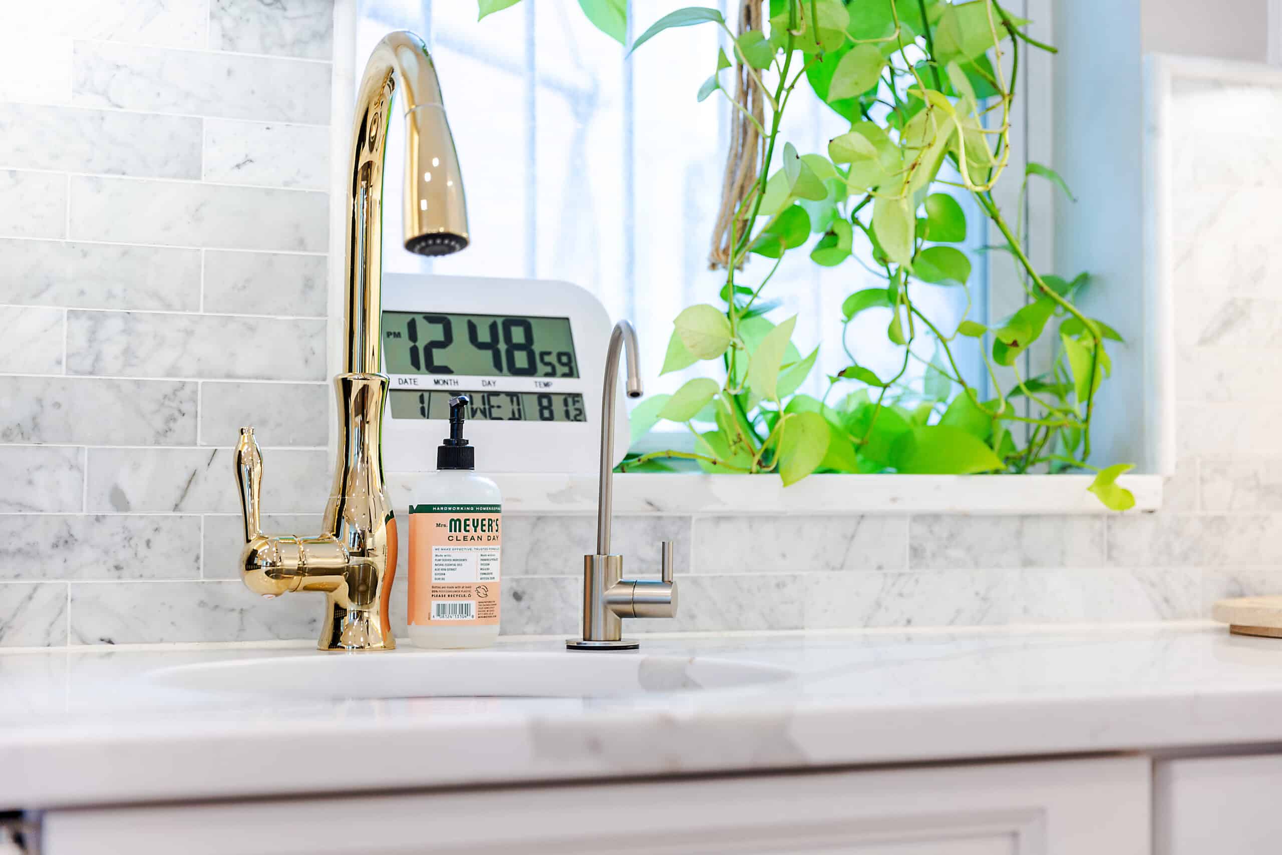 A white kitchen sink with a clock and a faucet