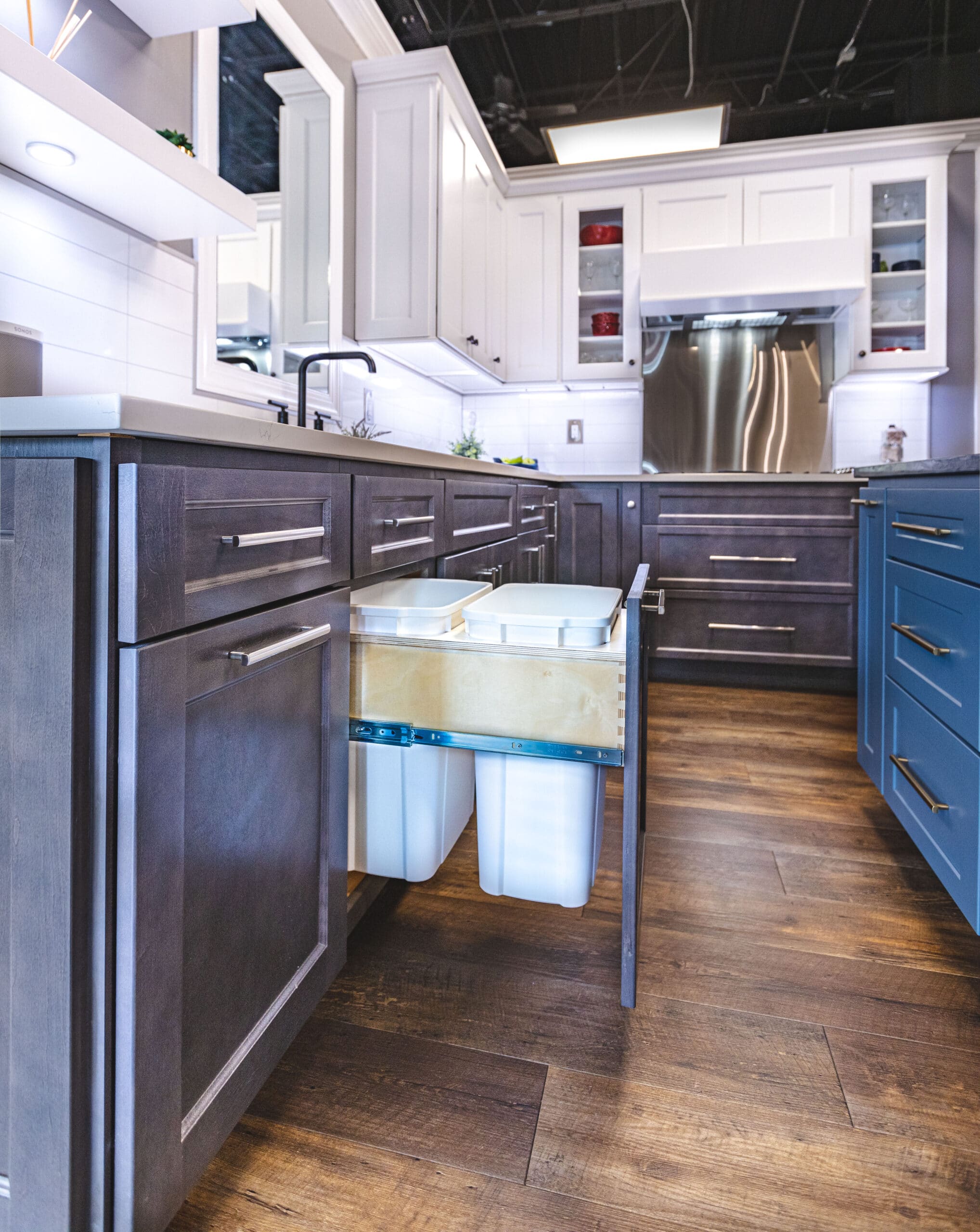 A kitchen with blue and brown cabinets and a trash can