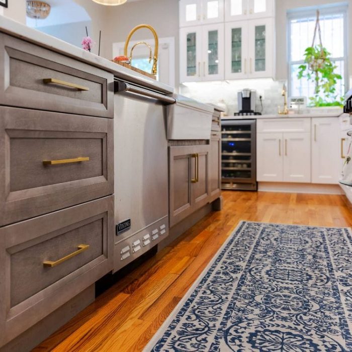 Open white Shaker cabinet revealing integrated double trash and recycling bins with gold hardware.