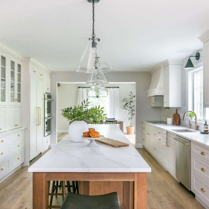 Expansive transitional kitchen featuring a dark wood island, double wall ovens, custom white range hood, and view into the dining room.