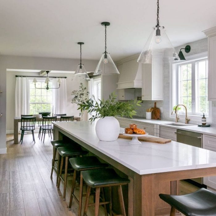 Open-concept kitchen with dark wood island, green leather bar stools, glass pendant lights, and view into the dining room.