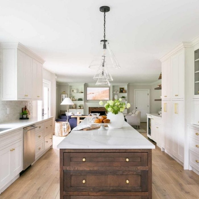 Open-concept transitional kitchen featuring a dark walnut island, white Shaker cabinets with gold cup pulls, and a view into the living room.