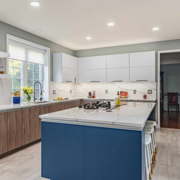 Complete modern kitchen remodel in Fairfax featuring a navy blue island with gas cooktop, two-tone white and wood cabinetry, and full-height quartz backsplash.