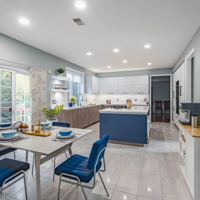 Modern open-concept kitchen with navy blue island, two-tone white and wood cabinets, and matching blue dining chairs.