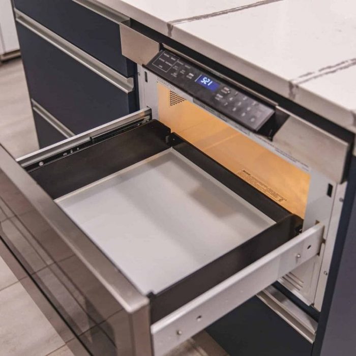 Open stainless steel microwave drawer installed in a navy blue kitchen island with white quartz countertops in Fairfax.