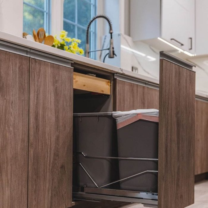 Modern Fairfax kitchen featuring a pull-out double trash and recycling cabinet with textured wood flat-panel doors and aluminum channel handles.