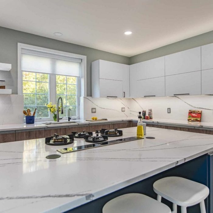 Modern Fairfax kitchen featuring floating shelves with integrated lighting, navy island with gas cooktop, and full-height quartz backsplash.