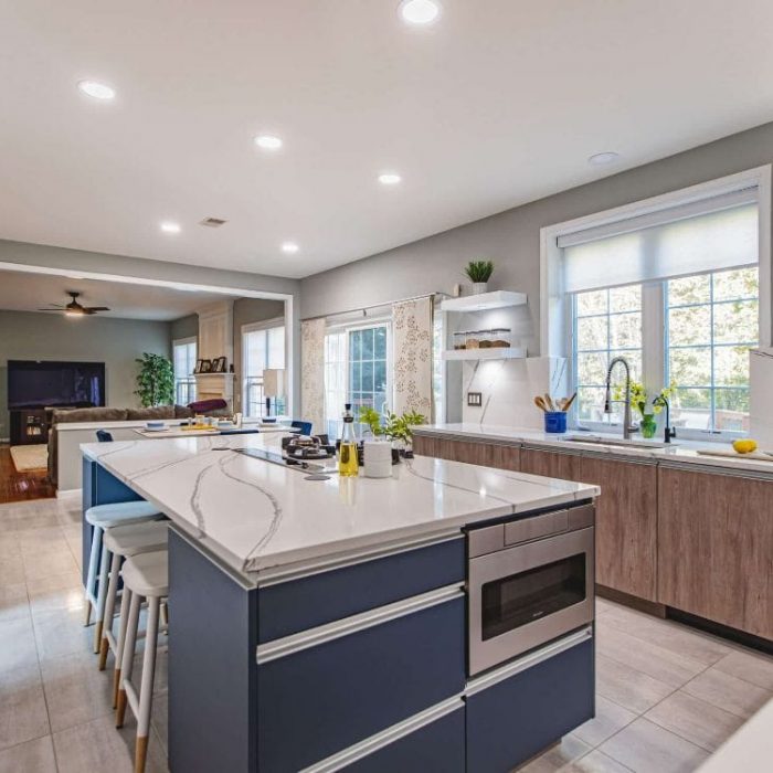Modern kitchen featuring a navy blue island with microwave drawer, wood grain flat-panel cabinets, and view into the living room.