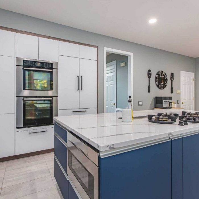 Modern kitchen remodel in Fairfax featuring a navy blue island with gas cooktop, double wall ovens, and white flat-panel cabinets.