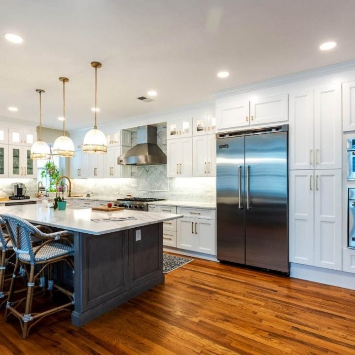 Luxury transitional kitchen with white floor-to-ceiling Shaker cabinets, a grey island, gold pendant lights, and blue woven stools.