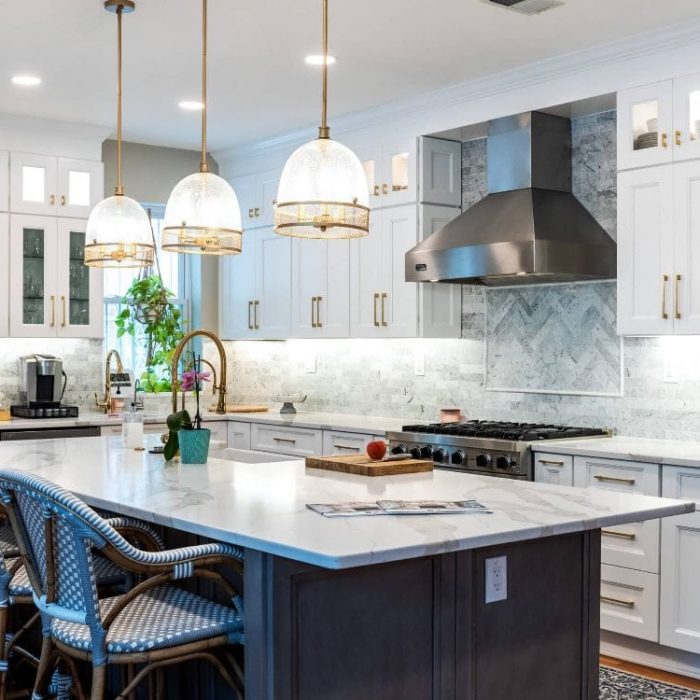 Luxury transitional kitchen with white Shaker cabinets, a grey island, gold hardware, and blue woven bistro stools.
