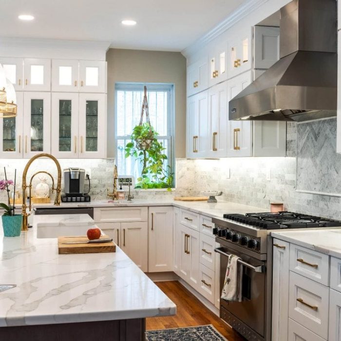 Luxury transitional kitchen featuring a marble quartz island, gold pendant lights, white Shaker cabinets, and a professional stainless steel range hood.