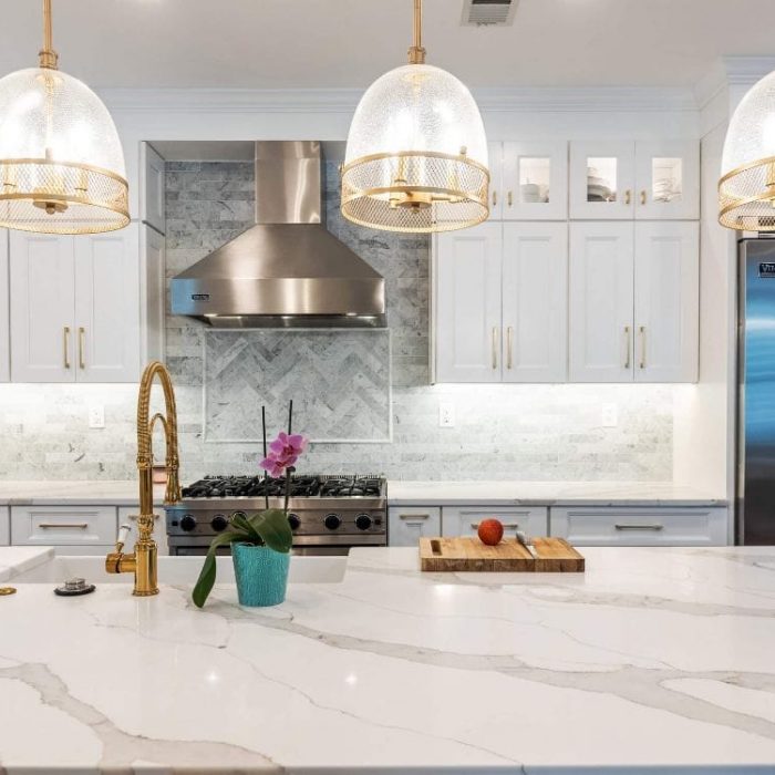 Integrated kitchen wall featuring a stainless steel refrigerator, stacked wall ovens, and an open white Shaker pantry with wooden pull-out trays.