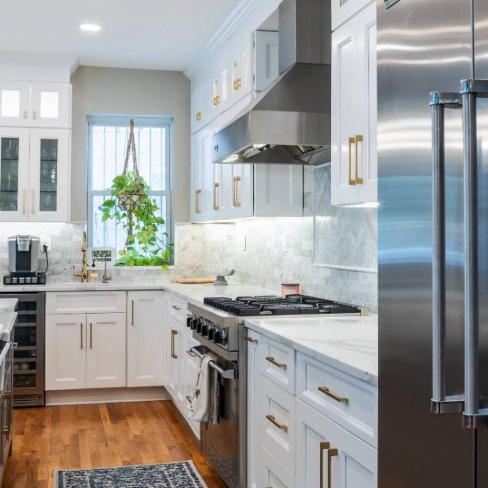 Integrated kitchen wall featuring a stainless steel Viking refrigerator, stacked wall ovens, and an open white Shaker pantry with wooden pull-out trays.