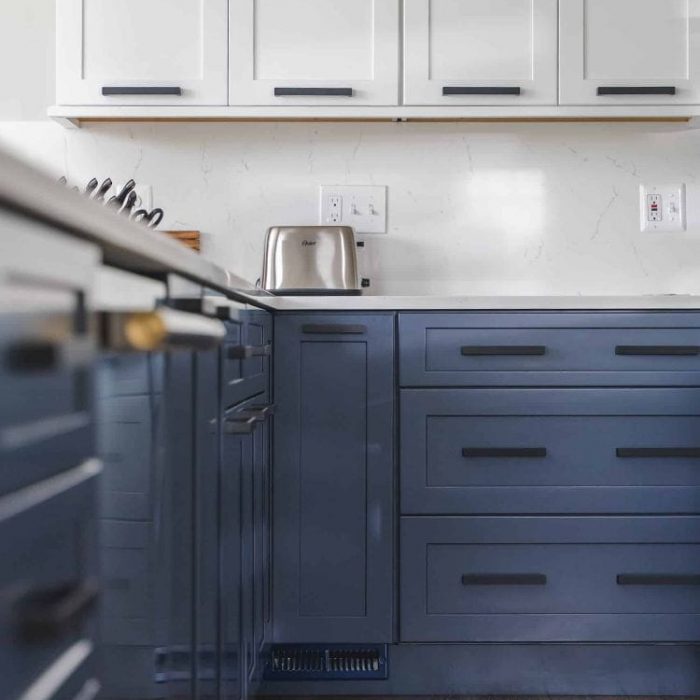 Close-up of navy blue base cabinets and white Shaker uppers with matte black pulls and a white quartz backsplash.