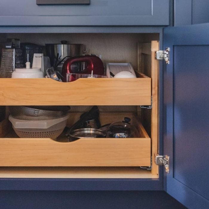 Open navy blue Shaker cabinet in a Leesburg kitchen featuring tiered wooden pull-out storage trays and matte black hardware.