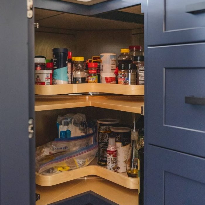 Navy blue corner kitchen cabinet with a two-tiered wooden Lazy Susan for organized spice and bottle storage.