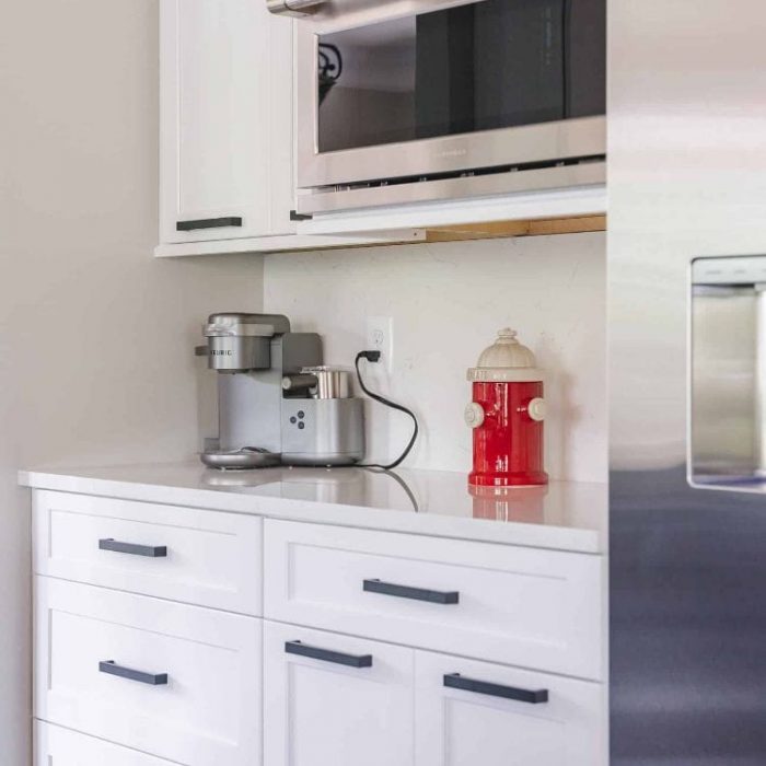 Coffee station with white Shaker cabinets, built-in microwave, quartz counters, and a red fire hydrant cookie jar.