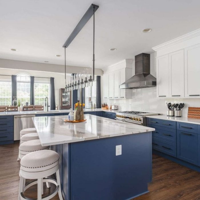Luxury kitchen remodel in Leesburg, VA featuring navy blue and white Shaker cabinetry, a marble-patterned island, and black industrial fixtures.