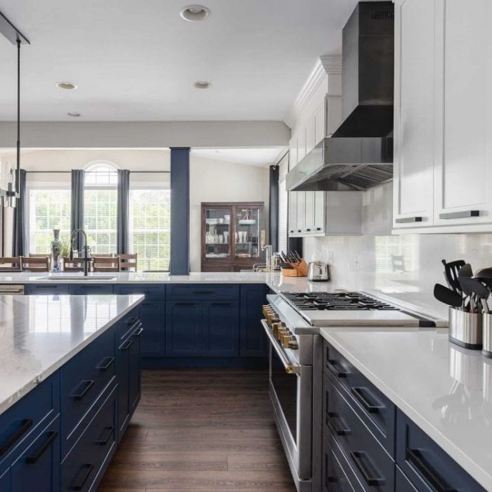 Modern Leesburg kitchen featuring navy blue base cabinets, white Shaker uppers, marble quartz counters, and a black industrial hood.
