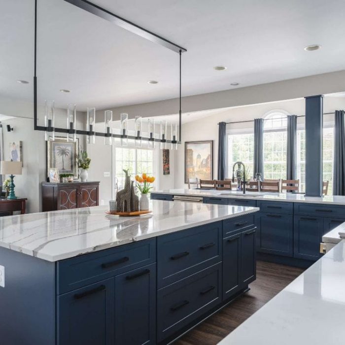 Leesburg open-concept kitchen with navy blue island, white Shaker cabinets, quartz counters, and linear black chandelier.