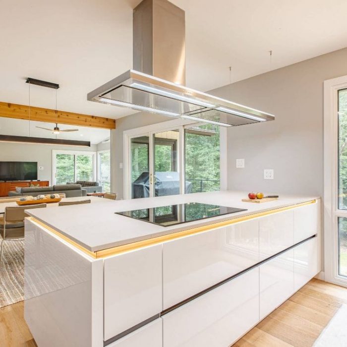 Modern white glossy kitchen island with induction cooktop, stainless steel T-hood, and LED accent lighting in an open home.