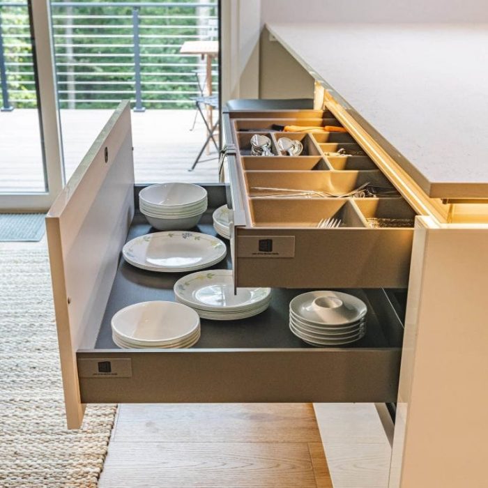 Open double-tiered kitchen drawer with cutlery organizer and stacked plates, featuring glossy white panels and integrated LED lighting.