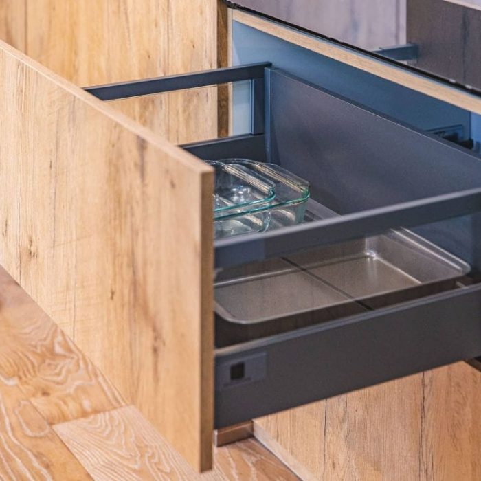 Modern wood-grain kitchen drawer with a sleek metal Legrabox system organized with glass and metal bakeware.