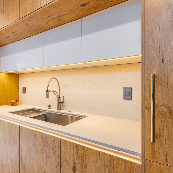 Modern kitchen workstation with wood-grain and white cabinetry, integrated LED lighting, and a professional stainless steel sink.